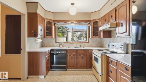 Kitchen featuring wood cabinetry, white countertops, a mosaic tile backsplash, a double basin sink, and a built-in dishwasher - 7408 40 Avenue, Edmonton, AB 
