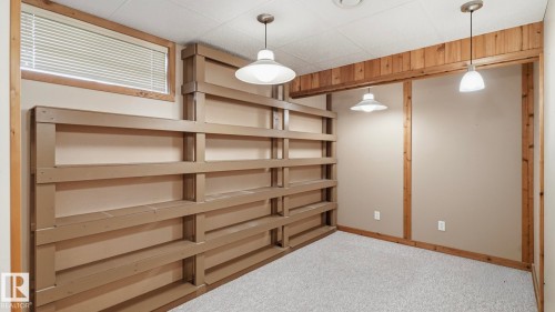 Room featuring extensive built-in shelving, plush carpeting, wood-paneled accents, a window with blinds, and multiple pendant light fixtures - 7408 40 Avenue, Edmonton, AB 