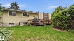 Rear exterior featuring a wood deck, mature landscaping, and a manicured lawn - 