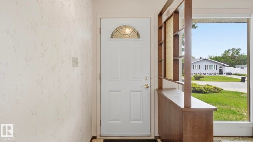 Entryway featuring a white paneled door with an arched transom window, a built-in wood-finish room divider with shelving, and large windows revealing an exterior landscape - 7408 40 Avenue, Edmonton, AB 