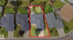 Property featuring a dark shingle roof, a concrete driveway, and a partially fenced backyard with mature trees - 