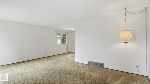 White painted walls, neutral carpeting, and a window with white trim - 7408 40 Avenue, Edmonton, AB 