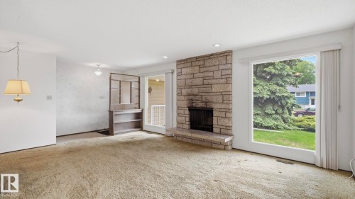 Living area featuring a stone-clad fireplace, large picture window, and built-in shelving unit - 7408 40 Avenue, Edmonton, AB 