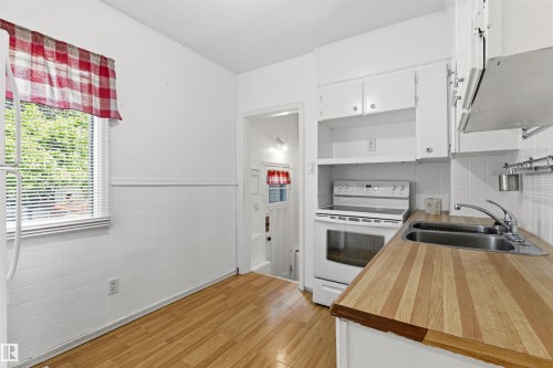 Kitchen featuring wood-finish flooring, white cabinetry, a double basin stainless steel sink, and a white electric range - 11417 65 Street, Edmonton, AB 
