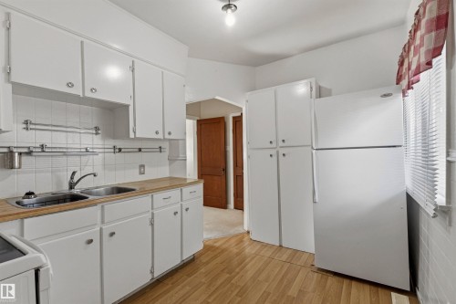 Kitchen featuring light wood-finish flooring, white cabinetry, and a tile backsplash - 11417 65 Street, Edmonton, AB 