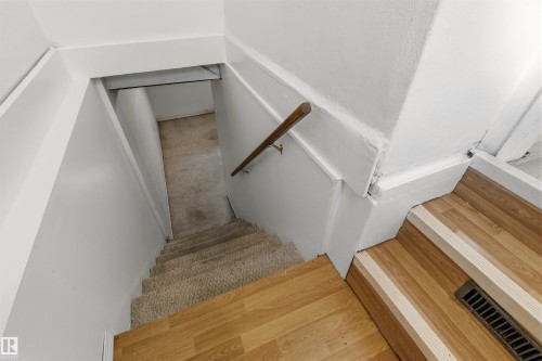 Staircase featuring wood-finish flooring, a carpeted lower section, a wooden handrail, and white painted walls - 11417 65 Street, Edmonton, AB 