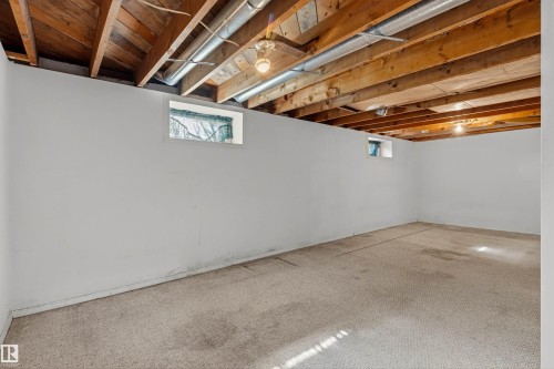 Spacious lower level with exposed wood joists and ductwork, featuring white painted walls, a light-toned carpeted floor, and multiple small windows - 11417 65 Street, Edmonton, AB 