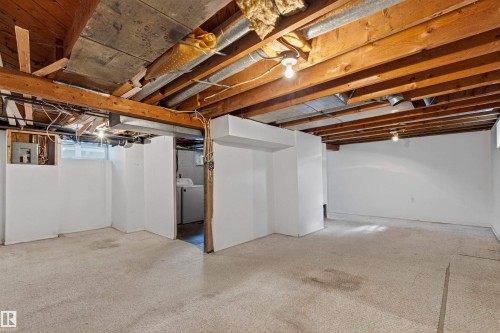 Unfinished basement space featuring exposed wooden ceiling joists, white painted walls, and light-colored carpet - 11417 65 Street, Edmonton, AB 