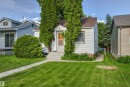 White siding exterior with a brown shingle roof, established front lawn, concrete walk, and mature trees framing the entrance - 11417 65 Street, Edmonton, AB 