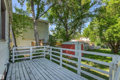 Outdoor deck area featuring white painted railings, a red storage shed, a green lawn, and mature trees - 11417 65 Street, Edmonton, AB 