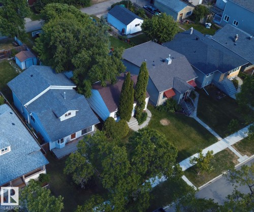 Single-family home featuring a gray shingle roof, red awnings, and a well-maintained front lawn with mature trees and a concrete pathway leading to the entrance - 11417 65 Street, Edmonton, AB 