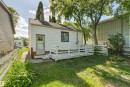 Rear exterior featuring white siding, a small deck, mature trees, and a partial fence - 11417 65 Street, Edmonton, AB 