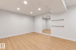Bright interior space featuring wood-finish flooring, recessed lighting, a large wall-mounted mirror, and two parallel wall bars - 