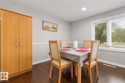 Dining area featuring dark wood-finish flooring, light grey walls with white chair rail molding, and a large window providing natural light - 11234 40 Avenue, Edmonton, AB 
