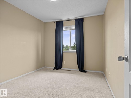 Carpeted room featuring a white window frame, light beige wall paint, white baseboards, and a semi-flush ceiling light - #88 5001 62 St, Beaumont, AB - Indoor