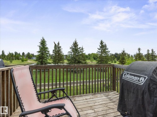 Outdoor wood deck with natural wood railings, overlooking a green landscape with mature evergreen trees and a body of water - #88 5001 62 St, Beaumont, AB - Outdoor With Deck Patio Veranda