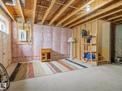 Unfinished lower level featuring concrete flooring, exposed ceiling joists, insulated walls, and an electrical service panel - 