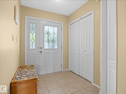 Entryway featuring a white paneled front door with decorative glass inserts, a coordinating sidelight, ceramic tile flooring, and two white bi-fold closet doors - 