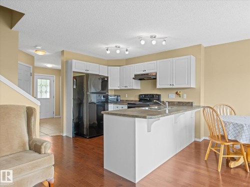 Kitchen featuring white cabinetry, dark wood-finish flooring, and a breakfast bar with an integrated sink - #88 5001 62 St, Beaumont, AB - Indoor Photo Showing Kitchen