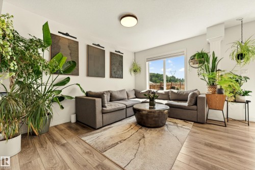Living area featuring light wood-finish flooring, white walls, a large window, a ceiling-mounted light fixture, and decorative wall art - 20507 128 Avenue, Edmonton, AB 