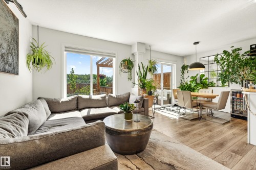 Open-concept living area featuring wood-finish flooring, white walls, and a large sliding glass door with an exterior wood pergola - 20507 128 Avenue, Edmonton, AB 