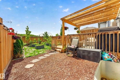 Fenced backyard featuring a wooden deck with a slatted pergola, a stepping stone pathway, and raised garden beds - 20507 128 Avenue, Edmonton, AB 