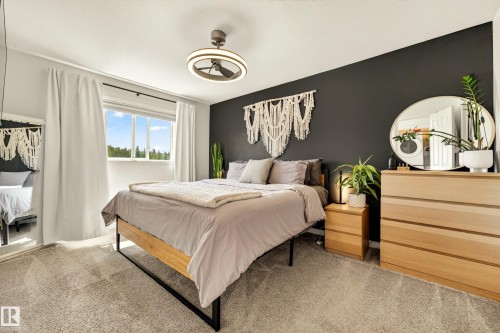 Spacious room featuring gray wall-to-wall carpeting, a large window with white trim, a modern ceiling fan with integrated lighting, and a dark accent wall - 20507 128 Avenue, Edmonton, AB 