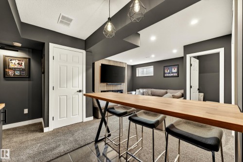 Entertainment area featuring an expansive wood-finish high-top bar with pendant lighting, dark gray walls, recessed ceiling lighting, and a neutral-toned carpet - 20507 128 Avenue, Edmonton, AB 