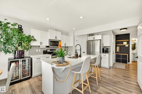 Bright kitchen featuring white shaker cabinetry, stainless steel appliances, a center island with countertop seating, wood-finish flooring, and recessed lighting - 20507 128 Avenue, Edmonton, AB 