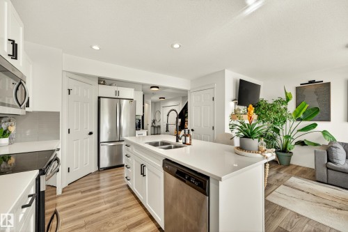 Open-concept kitchen featuring white cabinetry, light wood-finish flooring, a central island with an integrated sink, white countertops, and stainless steel appliances - 20507 128 Avenue, Edmonton, AB 