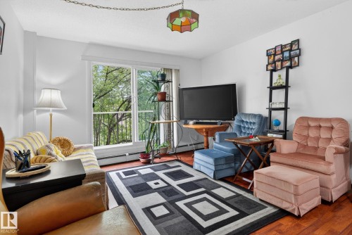 Hardwood-finish flooring featuring a geometric area rug, white walls, and a sliding glass door leading to a private balcony - 204 12404 114 Avenue, Edmonton, AB - Indoor Photo Showing Living Room