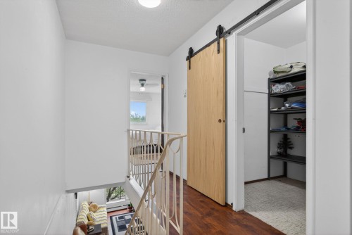 Upper-level hallway featuring wood-finish flooring, a contemporary barn door, and a built-in storage area with shelving - 204 12404 114 Avenue, Edmonton, AB - Indoor Photo Showing Other Room
