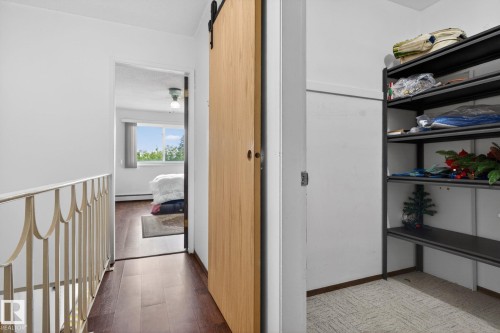Hallway with wood-finish flooring, a light-toned wood barn door, and a decorative metal railing - 204 12404 114 Avenue, Edmonton, AB - Indoor Photo Showing Other Room