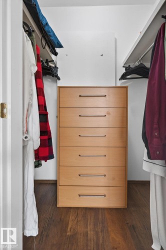 Walk-in closet featuring wood-finish flooring, a light wood-tone dresser with six drawers, and extensive built-in shelving with hanging rods - 204 12404 114 Avenue, Edmonton, AB - Indoor With Storage