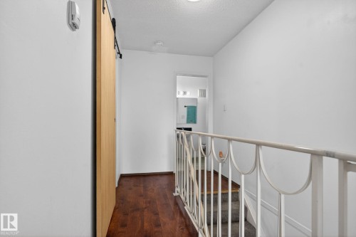 Upper-level hallway featuring wood-finish flooring, a contemporary barn door, and white walls - 204 12404 114 Avenue, Edmonton, AB - Indoor Photo Showing Other Room