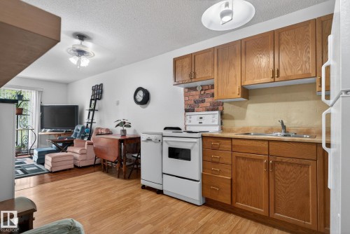 Kitchenette featuring wood cabinetry, white appliances, and a brick-patterned backsplash - 204 12404 114 Avenue, Edmonton, AB - Indoor Photo Showing Kitchen With Double Sink