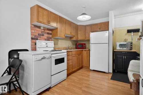Kitchen featuring wood-finish flooring, oak cabinetry, white appliances, a brick-look backsplash, and a pendant light fixture - 204 12404 114 Avenue, Edmonton, AB - Indoor Photo Showing Kitchen