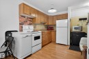 Kitchen featuring wood-finish flooring, oak cabinetry, white appliances, a brick-look backsplash, and a pendant light fixture - 204 12404 114 Avenue, Edmonton, AB  - Indoor Photo Showing Kitchen 