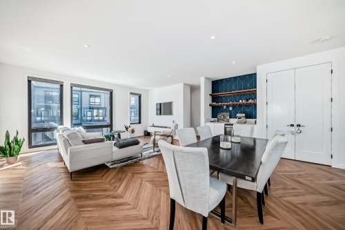 Open-concept living area featuring chevron wood-finish flooring, large multi-pane windows, a built-in beverage bar with open shelving and a geometric accent wall, and double panel doors - 46 1304 Rutherford Road, Edmonton, AB - Indoor
