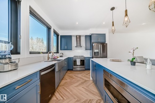 Modern kitchen featuring blue cabinetry, white countertops, stainless steel appliances, and wood-finish herringbone flooring - 46 1304 Rutherford Road, Edmonton, AB - Indoor Photo Showing Kitchen With Stainless Steel Kitchen With Upgraded Kitchen