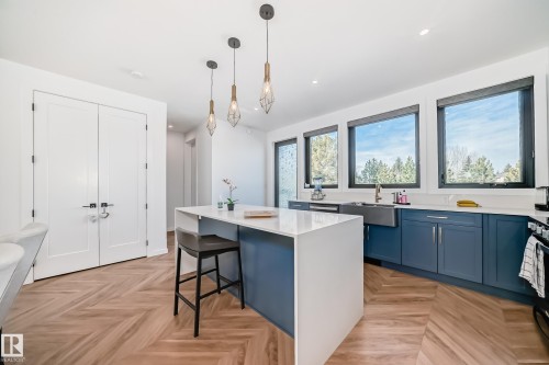Open-concept kitchen featuring an oversized island with seating, pendant lighting, herringbone wood-finish flooring, full-height white cabinetry, and a large farmhouse sink - 46 1304 Rutherford Road, Edmonton, AB - Indoor Photo Showing Kitchen With Upgraded Kitchen