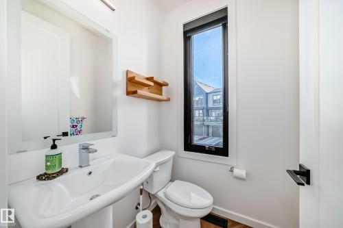 Contemporary bathroom featuring a pedestal sink with a chrome faucet, a rectangular mirror with backlighting, and a contrasting black-framed window - 46 1304 Rutherford Road, Edmonton, AB - Indoor Photo Showing Bathroom