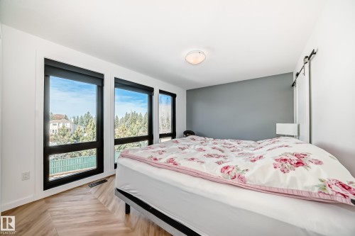 Room featuring light wood-finish flooring in a herringbone pattern, a prominent wall of black-framed windows, and a ceiling-mounted light fixture - 46 1304 Rutherford Road, Edmonton, AB - Indoor Photo Showing Bedroom