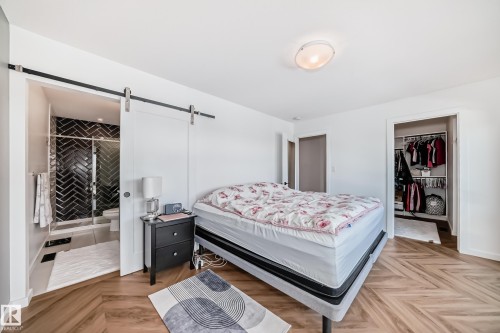 Bedroom featuring wood-finish herringbone flooring, a sliding barn door, and a dedicated closet space - 46 1304 Rutherford Road, Edmonton, AB - Indoor Photo Showing Bedroom