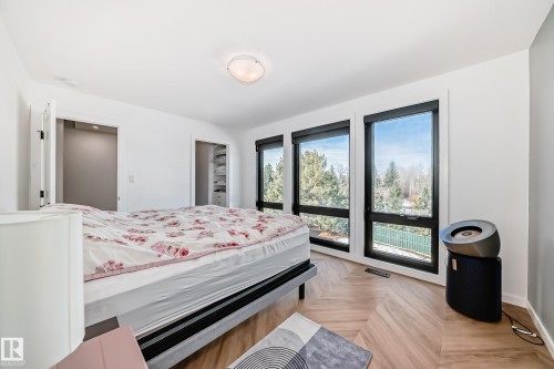 Room featuring herringbone wood-finish flooring, a series of three large windows with black frames, and white walls - 46 1304 Rutherford Road, Edmonton, AB - Indoor Photo Showing Bedroom