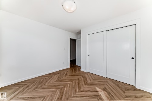 Room with chevron wood-finish flooring, white walls, and a pair of white sliding doors with black hardware - 46 1304 Rutherford Road, Edmonton, AB - Indoor Photo Showing Other Room