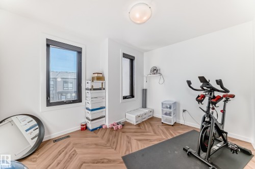 Room featuring wood-finish flooring in a herringbone pattern, white walls, and two black-framed windows - 46 1304 Rutherford Road, Edmonton, AB - Indoor Photo Showing Gym Room