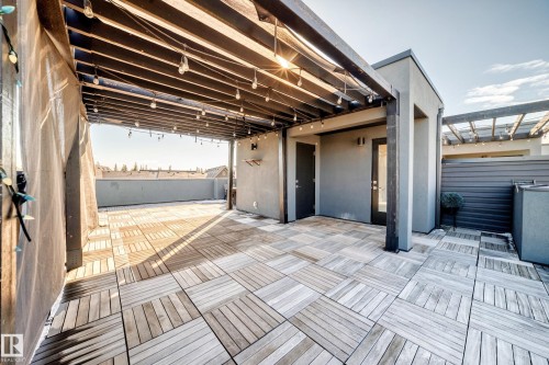Expansive rooftop patio featuring light-toned wood-finish deck tiles, a dark-stained wood pergola, and string lighting - 46 1304 Rutherford Road, Edmonton, AB -  With Exterior
