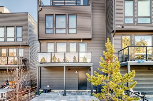 Rear exterior of a contemporary multi-story residence featuring horizontal siding, multiple balconies with glass panel railings, and a ground-level patio with stone pavers - 46 1304 Rutherford Road, Edmonton, AB - Outdoor With Exterior