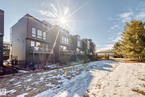 Contemporary multi-story exterior with dark horizontal siding, multiple balconies with glass railings, and a fenced perimeter - 46 1304 Rutherford Road, Edmonton, AB - Outdoor